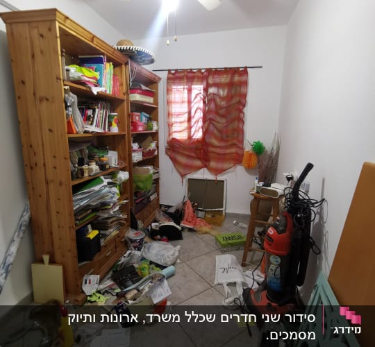 חדר מבולגן עם מדפים, שואב אבק וחפצים מפוזרים על הרצפה.
